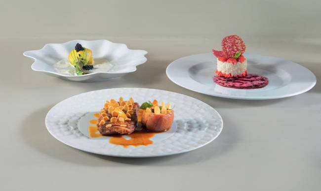 Président 022 Três pratos brancos de porcelana, contendo uma flor de abobrinha defumada sobre leite de coco, pato assado commaçã caramelada e arroz-doce com fava de baunilha