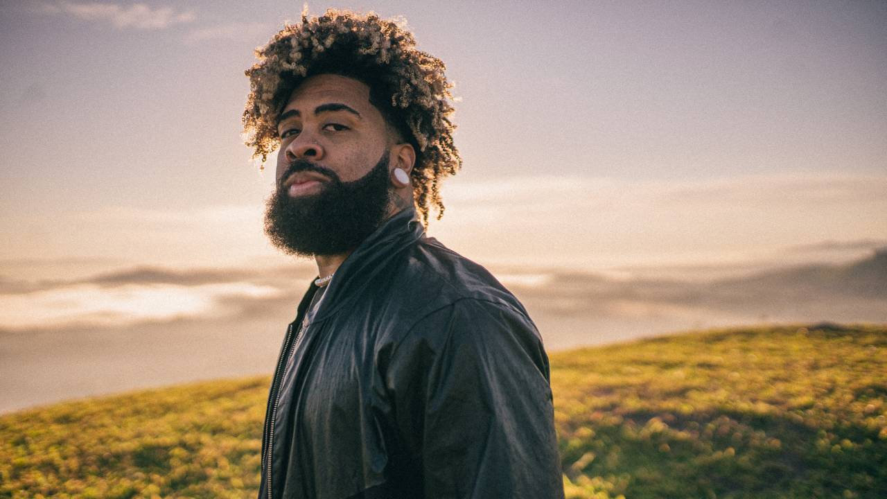 Imagem mostra homem de barba com um morro ao fundo