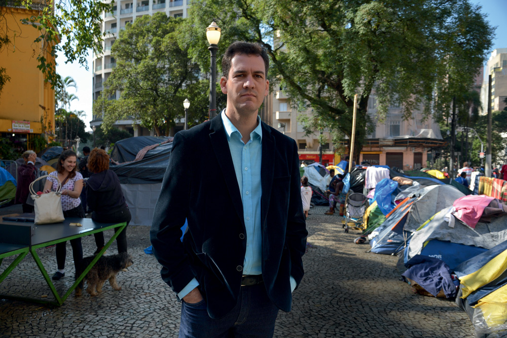 Ariel de Castro Alves é um senhor branco, magro, sem barba e de cabelos escuros. Está em pé no Centro de SP e posa sério para foto. Usa um terno preto