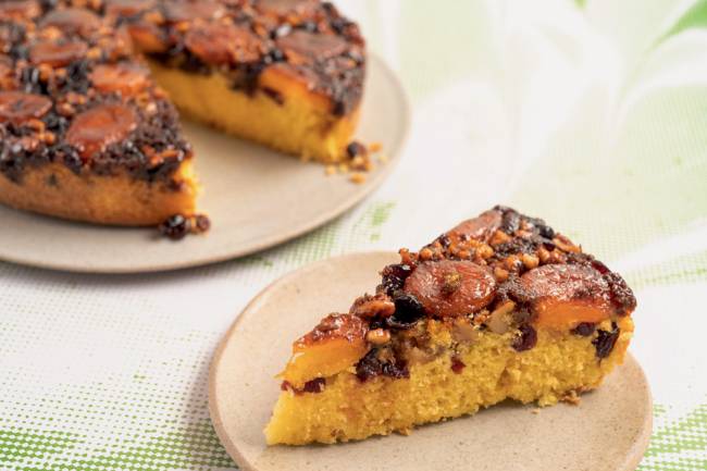 Bolo de laranja com damasco, nozes e cranberries Marilia Zylbersztajn Bolo de laranja sobre um prato faltando uma fatia, que está sobre um prato menor ao lado
