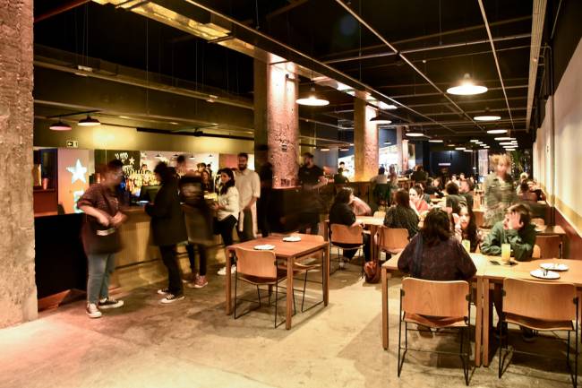Cineclube Cortina Ambiente interno de bar, com pessoas em pé e sentadas à mesa