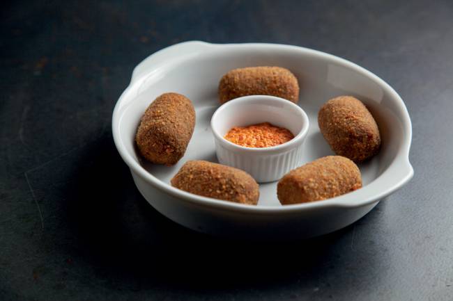 Prato alto de porcelana contendo cinco croquetes e um recipiente de porcelana ao meio com molho