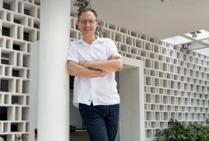 Imagem mostra homem de camisa branca, de braços cruzados, sorrindo