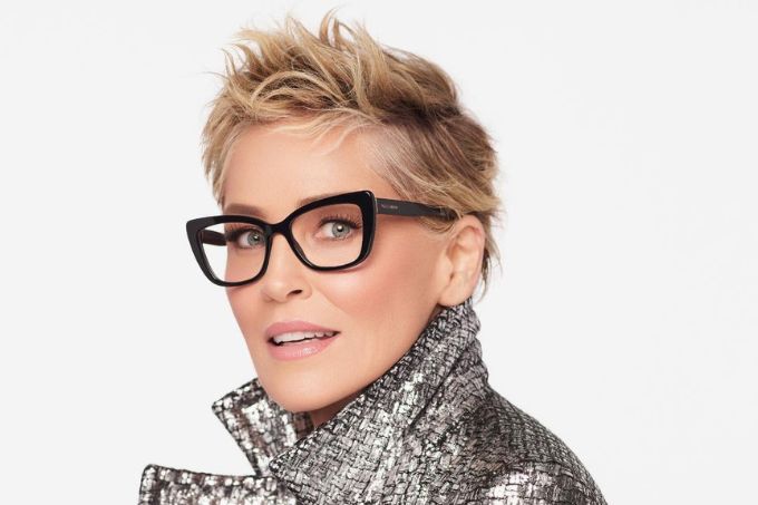 Foto de Sharon Stone usando óculos, cabelo curto e jaqueta prateada