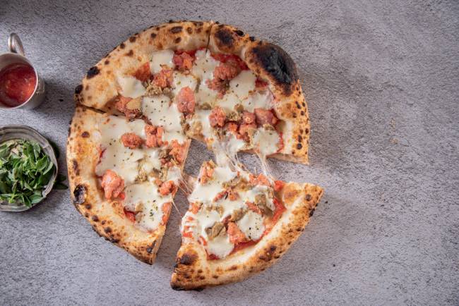 Foglia 029.jpg Pizza sobre superfície de pedra cortada em 4 pedaços, com um deles um pouco afastado dos demais