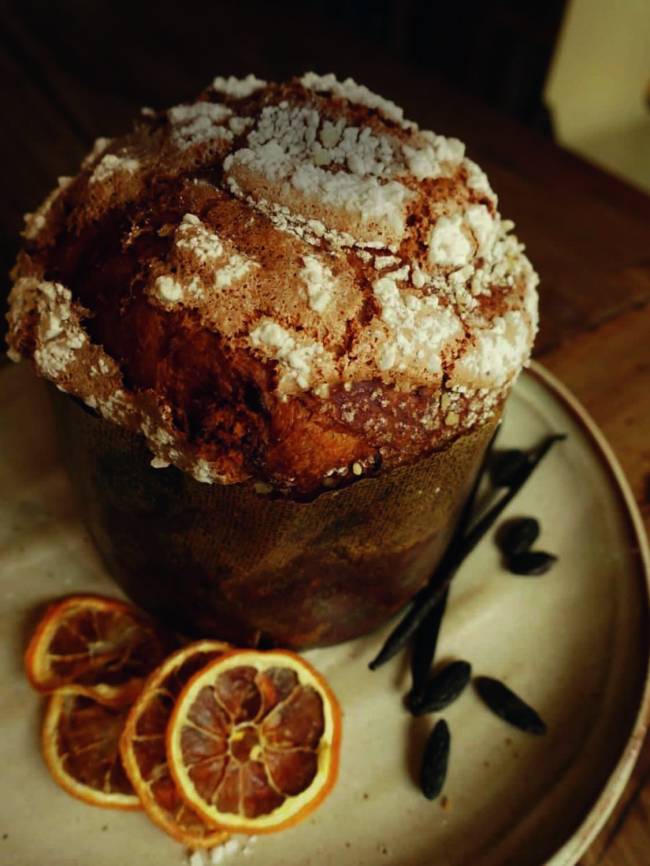 Panetone inteiro sobre prato onde há fatias de laranja desidratada