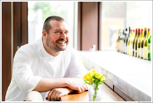 Pier Paolo Picchi sentado com jaleco de chef em frente a vaso de flores amarelas