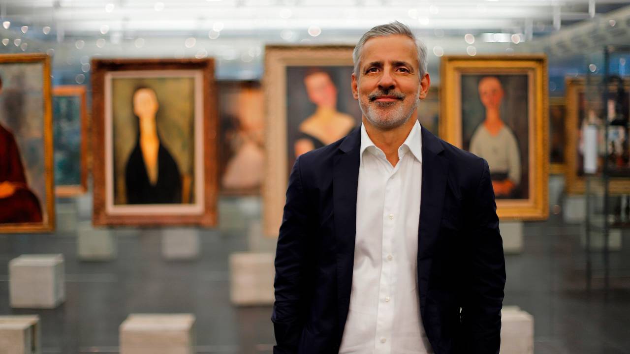 Foto de Adriano Pedrosa usando terno sem gravata, com cenário de obras de arte no Masp