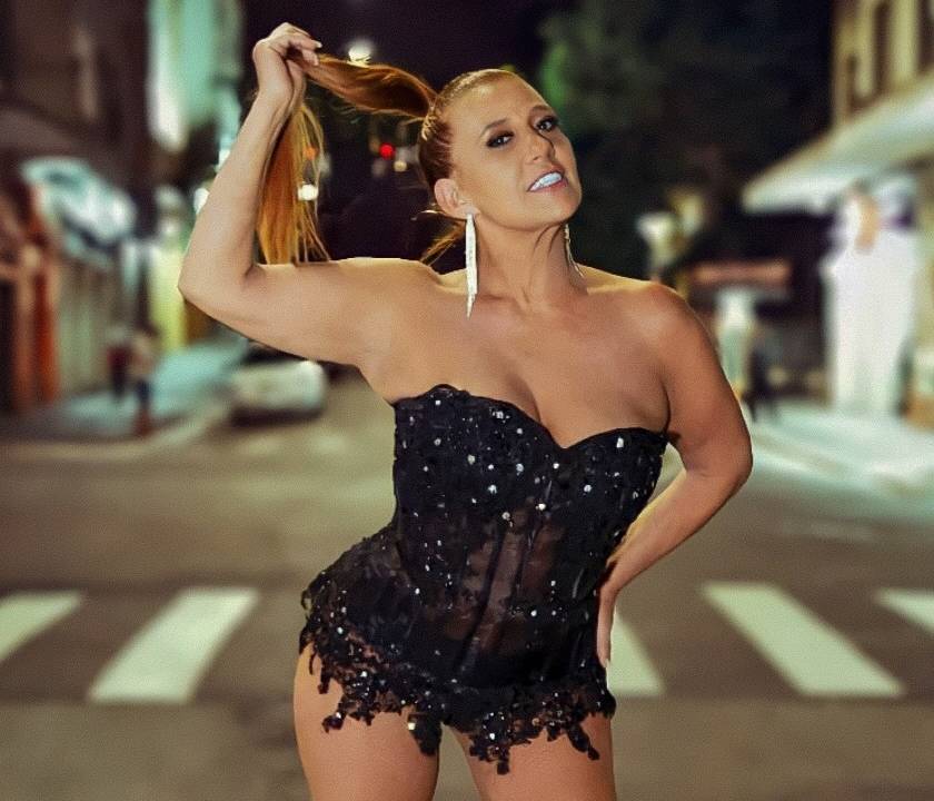 Rita Cadillac posa segurando rabo de cavalo no meio de avenida. Veste lingerie preta e exibe as pernas.