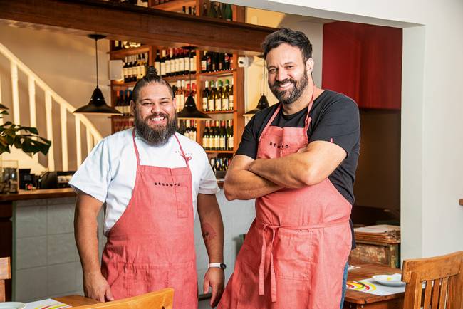 Lucas Silla e Marcelo Corrêa Bastos com aventais vermelho-rosados dentro do restaurante