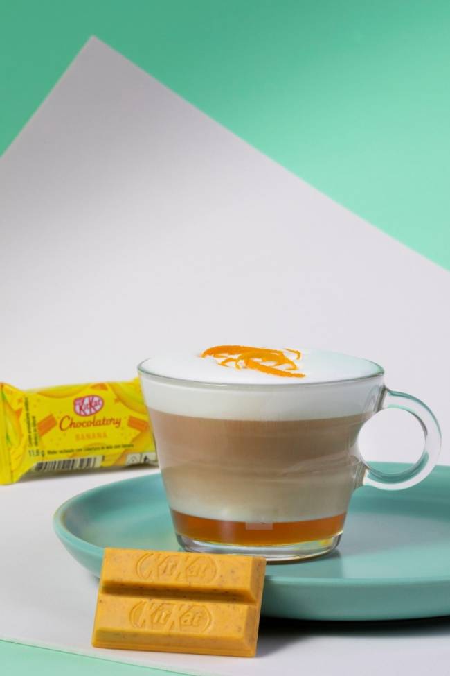cappuccino kit kat uma caneca de vidro com a bebida e um chocolate amarelo pequeno ao lado