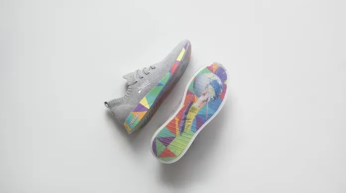 Foto exibe par de sapatos de tecido cinza com solado todo colorido.
