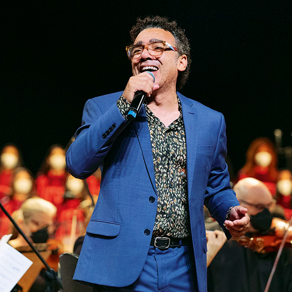 Simoninha Imagem mostr homem de terno azul cantando em palco