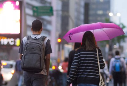 Duas pessoas de costas, andando na rua, e uma delas segurando um guarda-chuva rosa