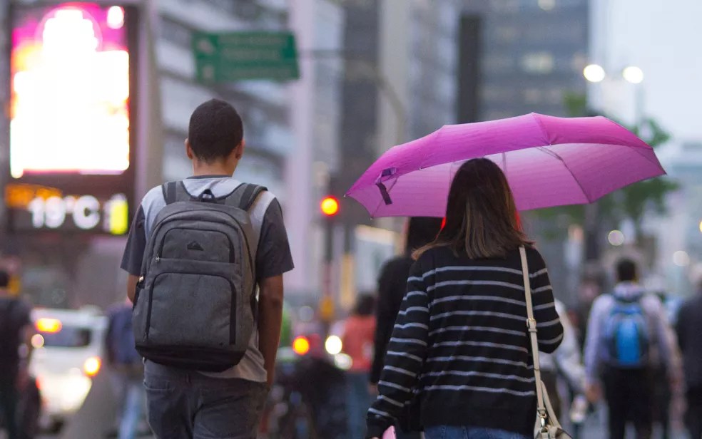 Duas pessoas de costas, andando na rua, e uma delas segurando um guarda-chuva rosa
