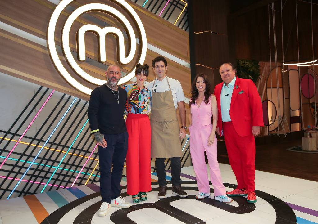 Cinco pessoas, sendo três homens com uma mulher entre eles, e o símbolo do MasterChef atrpas