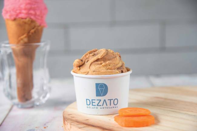 Dezato Em primeiro plano, pote de sorvete alaranjado com uma fatia de cenoura ao lado