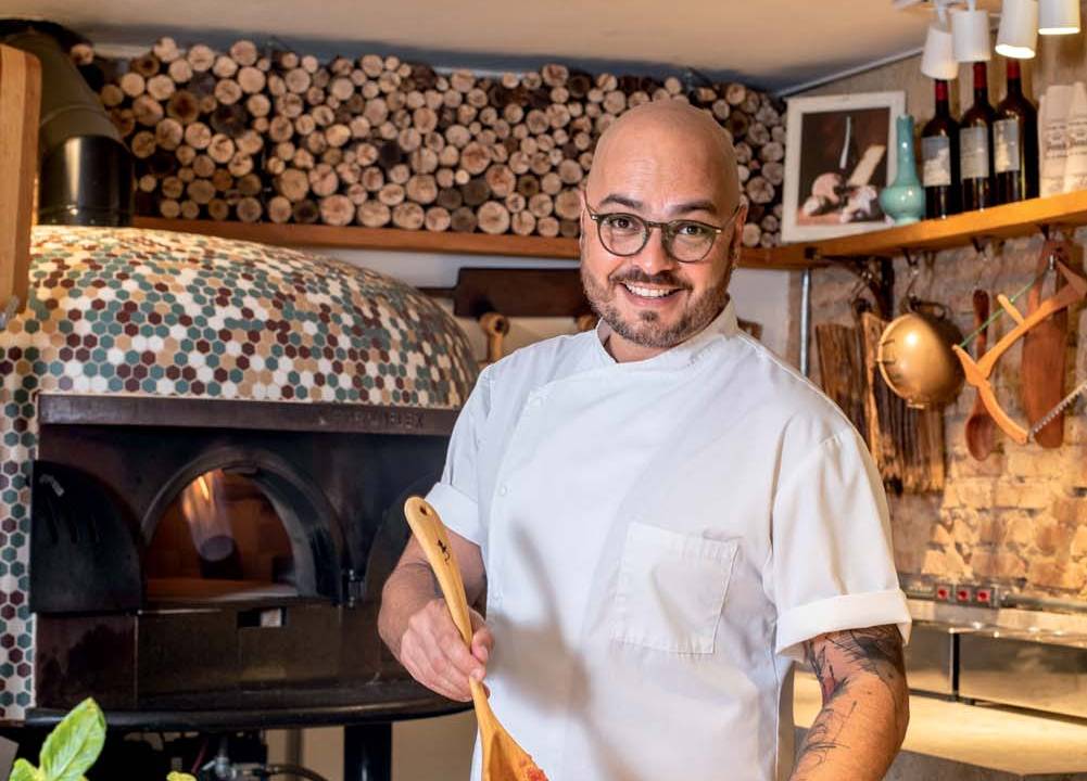 Diego Sacilotto coloca molho de tomate sobre massa de pizza aberta
