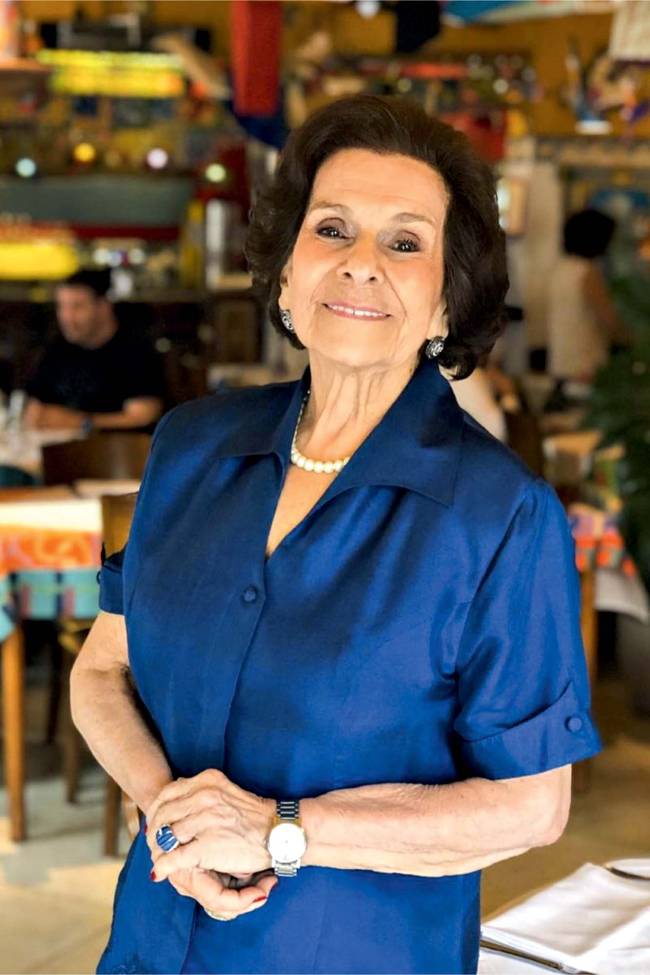Dona Bettina Orrico.jpg Senhora branca, de cabelos escuros e curtos, veste espécie de tailleur de mangas curtas azul royal e colar de pérolas, olha para a câmera com as mãos juntas