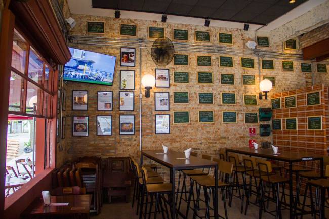 Esquina do Souza Vila Leopoldina Ambiente Ambiente interno de bar com tijolinhos à vista e quadros na parede, mesas e cadeiras e um telão de televisão no canto
