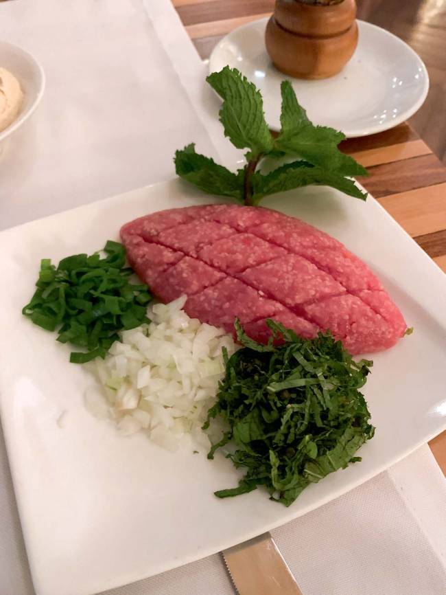 Quibe cru arábia Quibe cru, cebola picada, cebolinha picada e hortelã picado sobre prato branco de porcelana