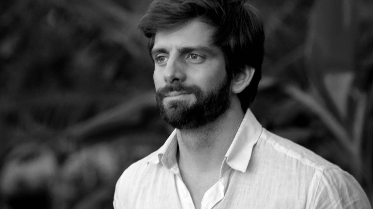 Foto em preto e branco exibe homem com barba vestindo camisa branca.