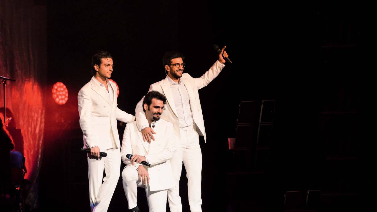 Imagem mostra três homens de roupas brancas em cima de palco