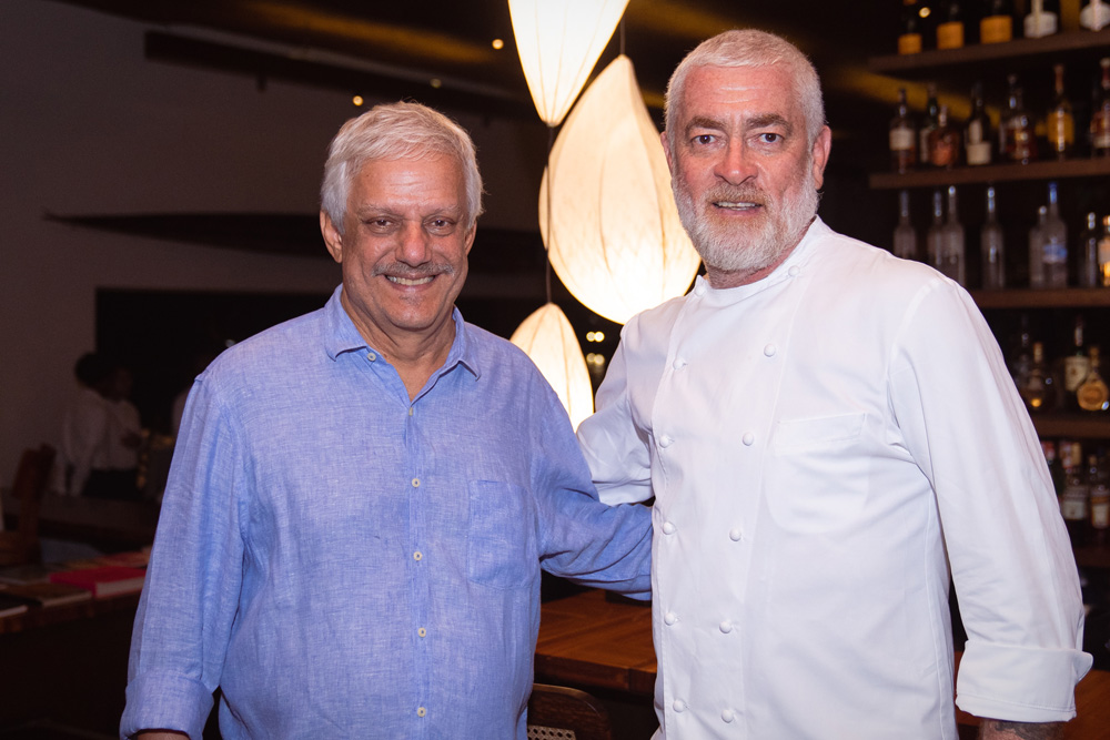 Dois homens de camisa azul e um de dolma um ao lado do outro se abraçam e posam para a foto