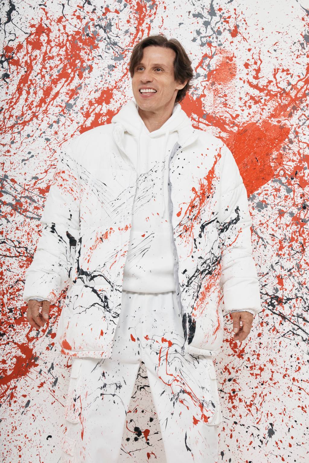 Caito Maia (Gil Inoue-Divulgação) Caito Maia posa com roupa branca manchada de tintas coloridas e parede borrada.
