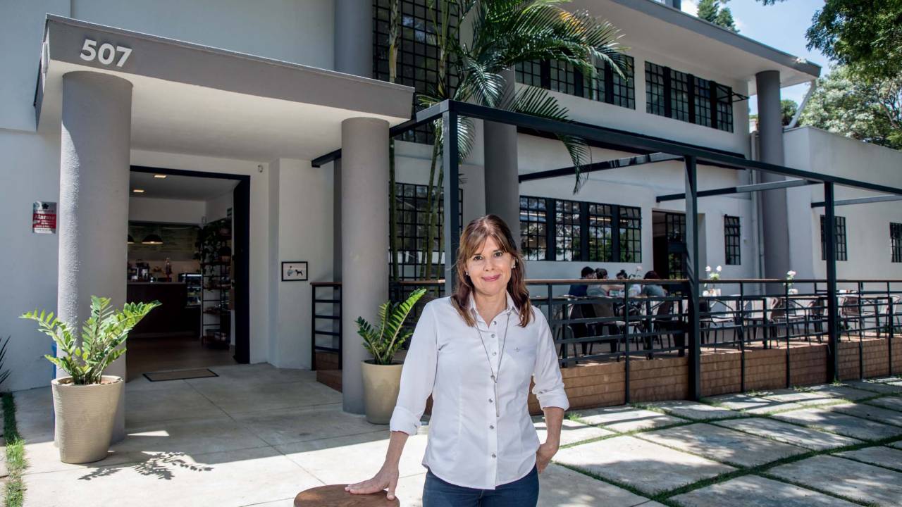 Mulher de pé vestindo camisa azul calça jeans de pé em frente à fachada da loja