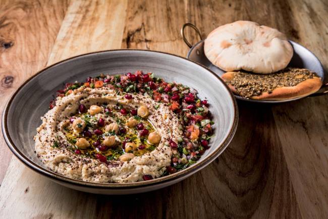 Tigela com homus ao lado de prato com esfirra de zaatar e pão feito na casa