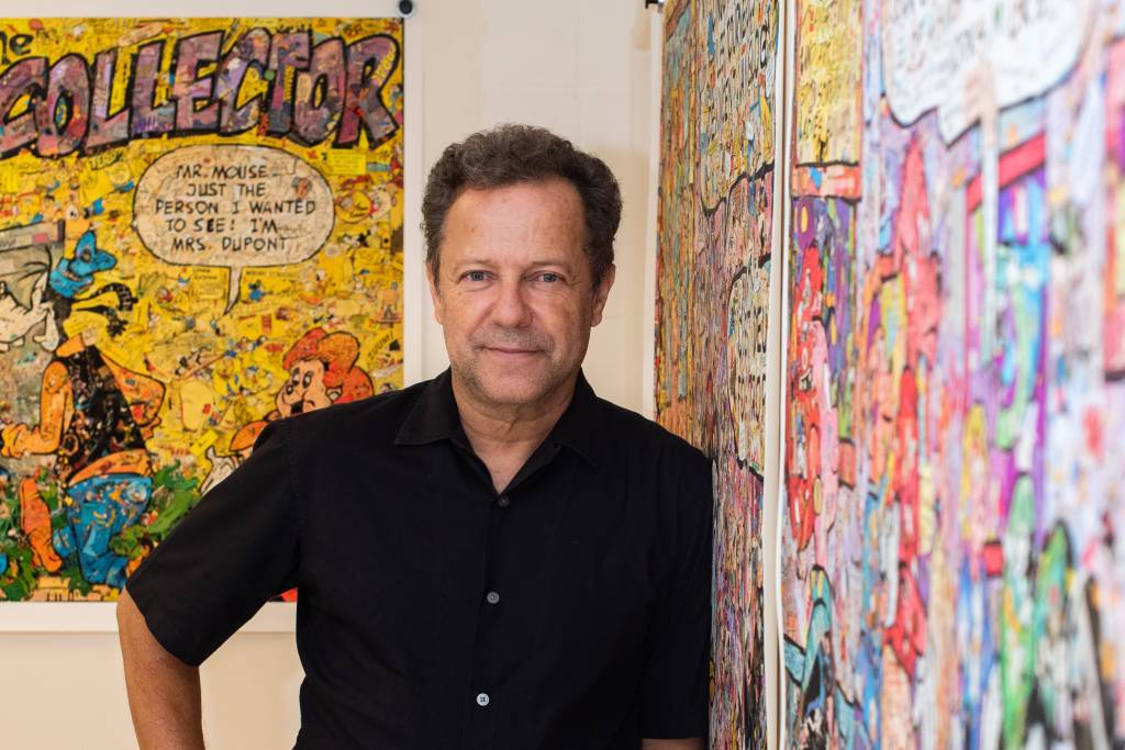 Imagem mostra homem de camisa preta apoiado em parede com quadro colorido