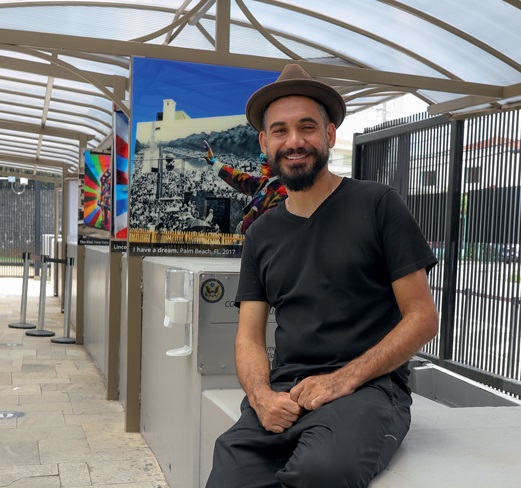Foto mostra Eduardo Kobra usando preto em frente a série de painéis com fotos de grafites