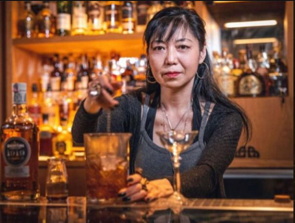 Mulher em balcão de bar misturando bebidas em um copo
