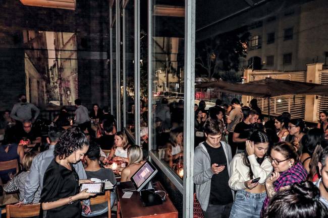 Moma fila lotado Itaim Bibi Ambiente interno de restaurante cheio com fila de espera do lado de fora da parede de vidro