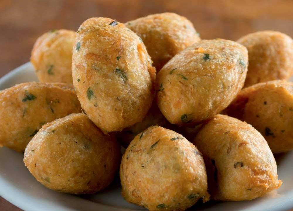 Prato de porcelana contendo bolinhos de bacalhau fritos sobre superfície de madeira