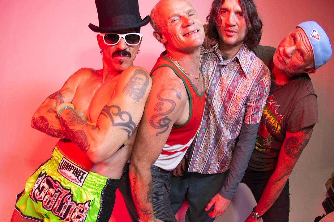 Imagem mostra quatro homens sorrindo, com roupas coloridas e luz rosa