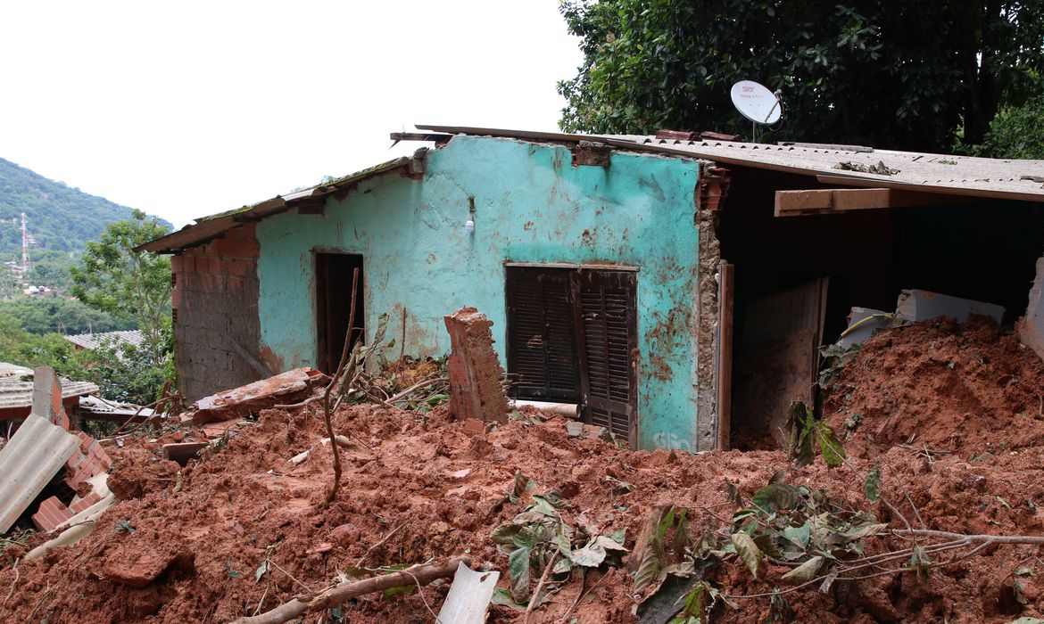 Foto mostra casa com parede verde destruída por lama, que chega a altura das janelas