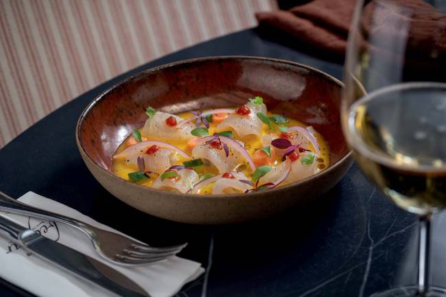 Ceviche de peixe branco Beefbar Cumbuca escura sobre mesa preta contendo ceviche de peixe branco, batata-doce, pepino, molho de maracujá e pimenta