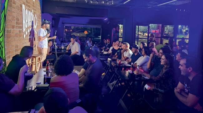 Beverly Comedy Homem fala em microfone no palco e pessoas sentadas o assistem