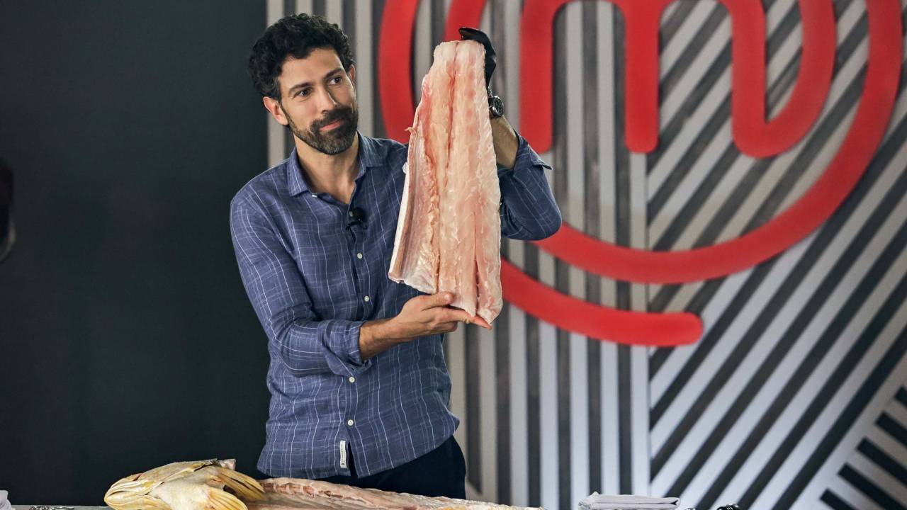 Homem veste camisa azul e segura peixe sem pele