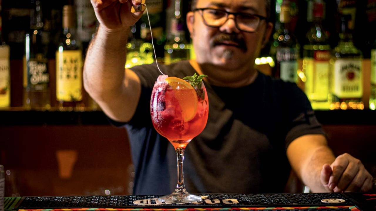 Bartender prepara drink laranja com taça alta sobre balcão