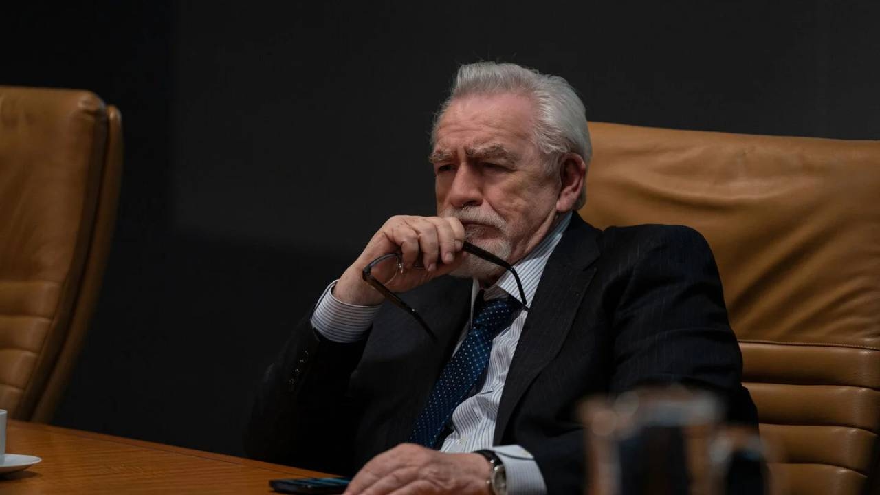 Logan Roy, de Succession, sentado em uma mesa com semblante preocupado