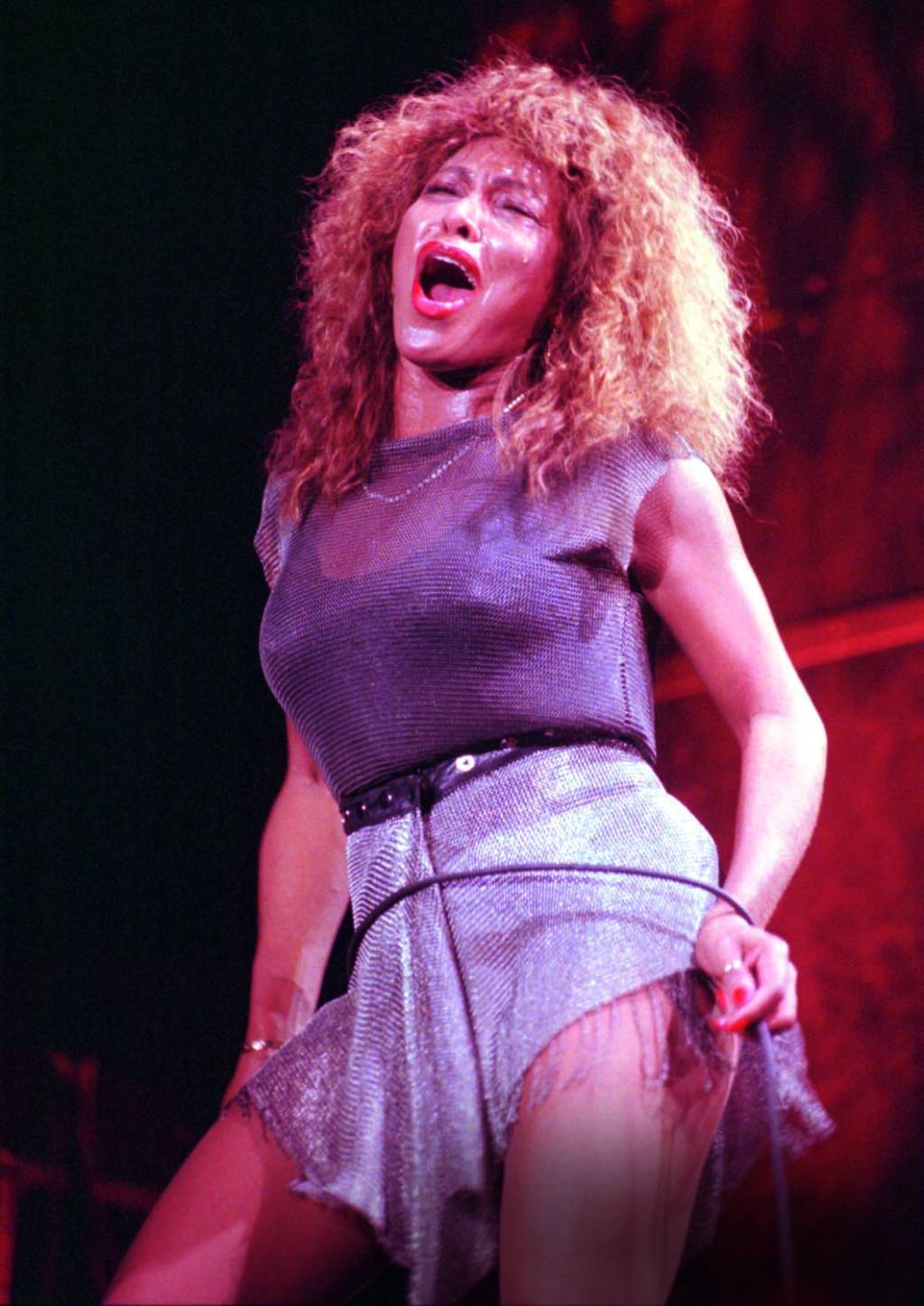 Tina TUrner Imagem mostra mulher em palco, com roupa brilhante e a boca aberta