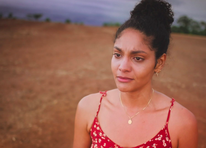 Uma mulher de cabelo preso e uma fazenda ao fundo