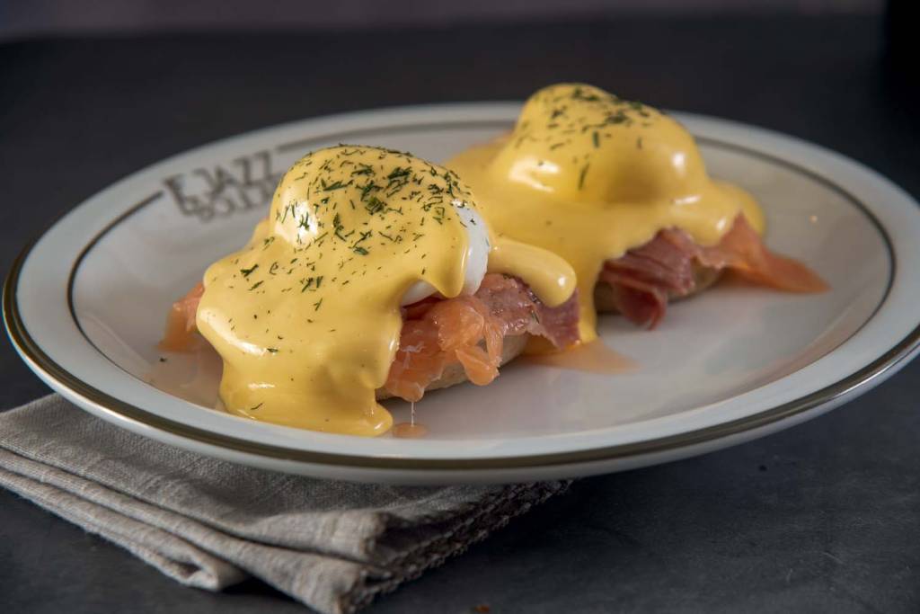 Le Jazz Boulangerie Dois ovos benedict com presunto e molho holandês lado a lado em prato de louça branca.