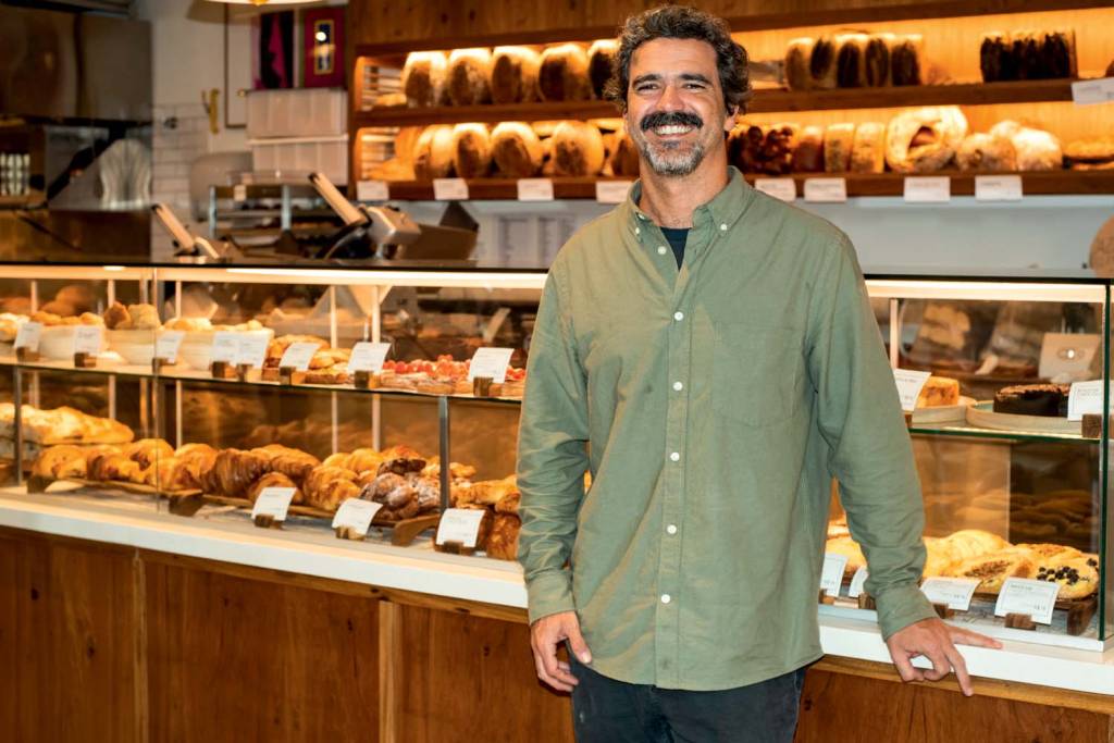 Le Jazz Boulangerie Homem branco de camisa verde em frente a vitrine de pães.