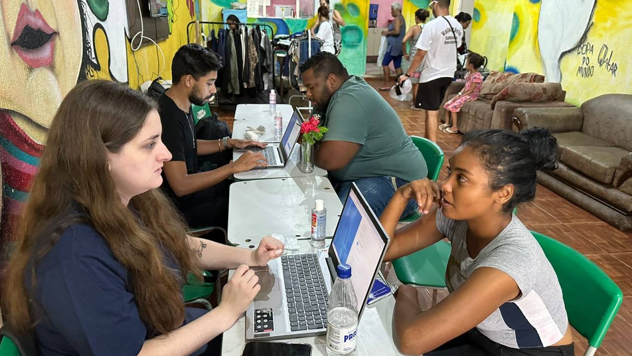 Sala grafitada com pessoas sendo entrevistadas em mesas atrás de laptops.