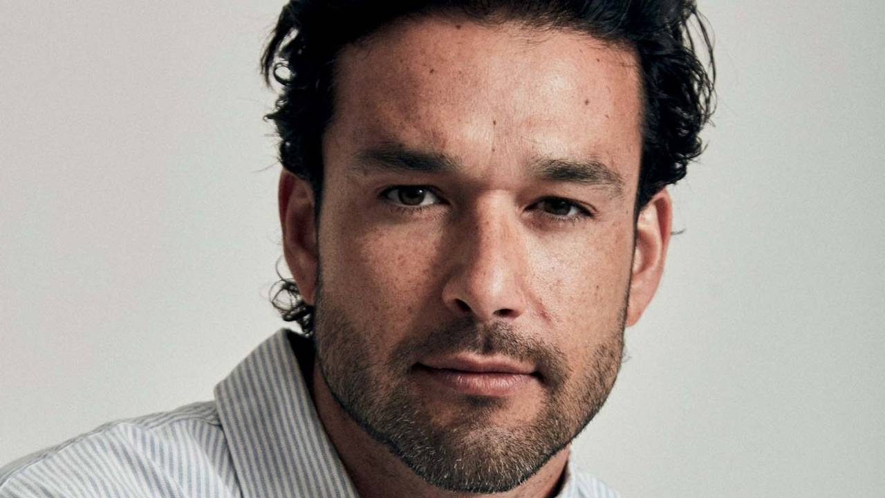 Homem branco encara a câmera. Tem barba por fazer e cabelos pretos.