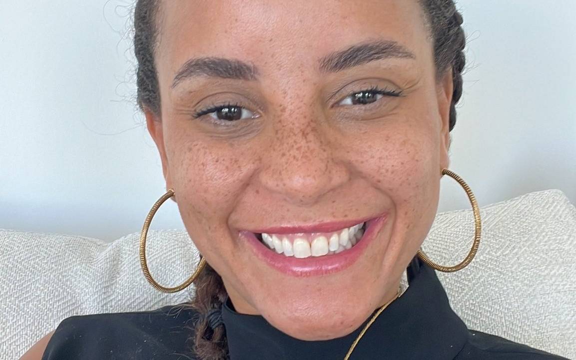 Mulher com o cabelo trançado, roupa preta e brincos de argolas douradas